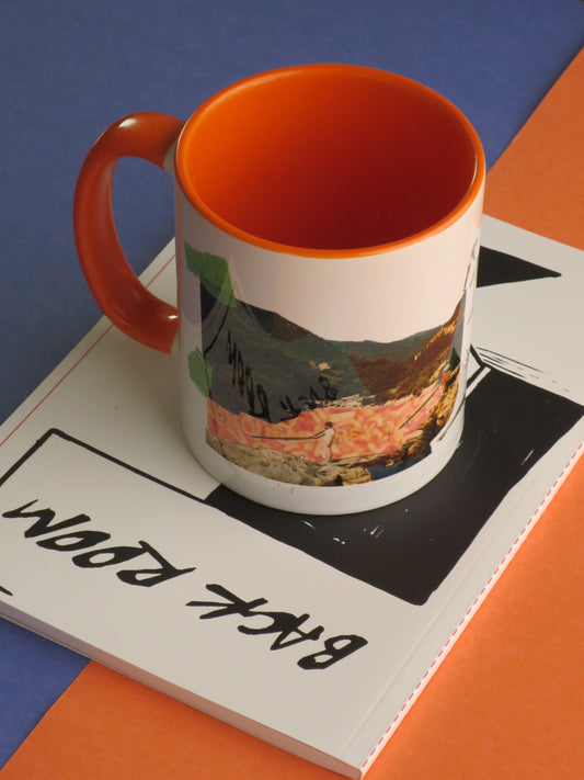 A white ceramic mug with a bright orange interior and handle, featuring a colourful landscape collage on the side, resting on a white book with black text (Back Room) against a blue and orange background.