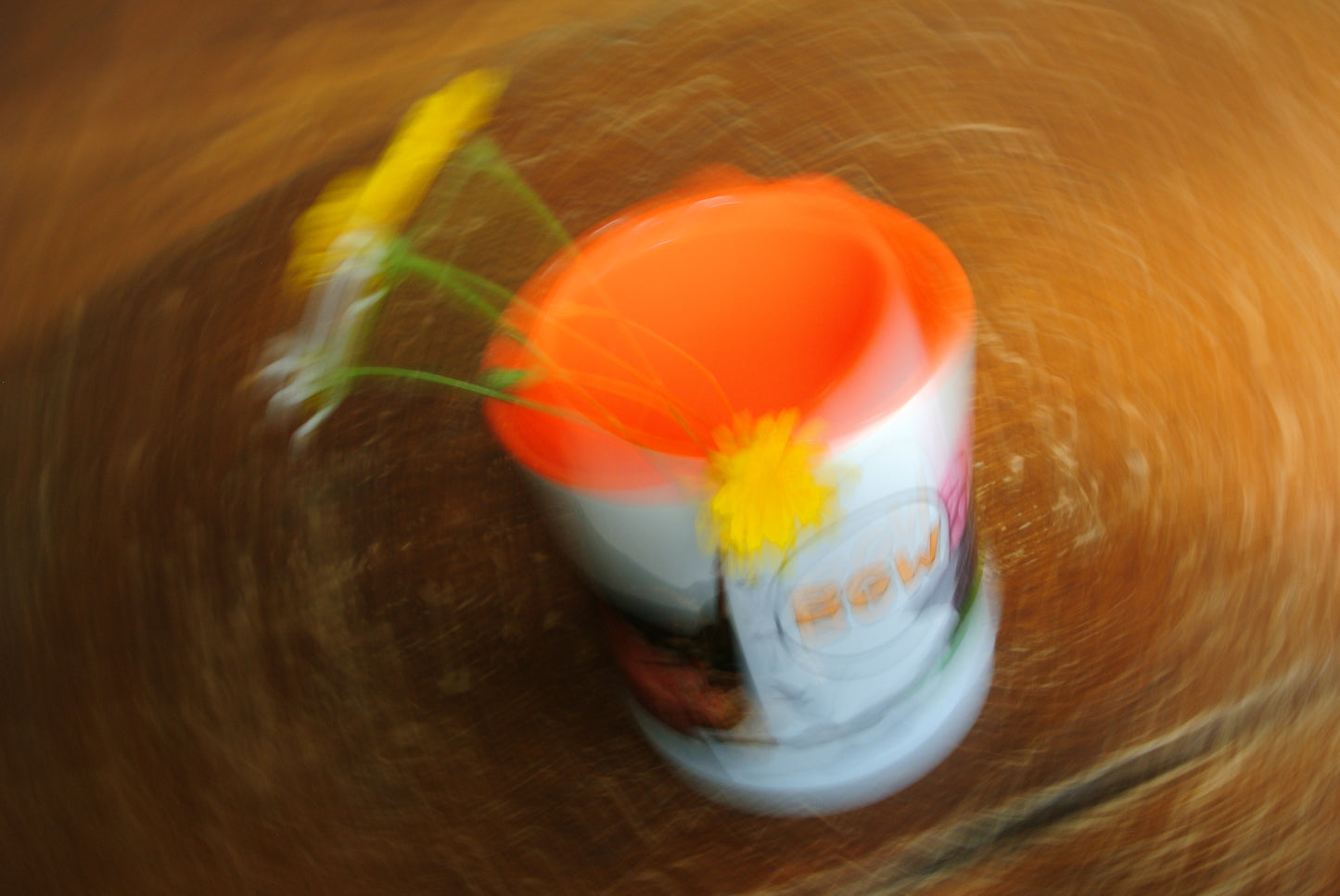A white cylindrical cup with a bright orange interior, decorated with yellow flowers, set against a heavily blurred brown background.